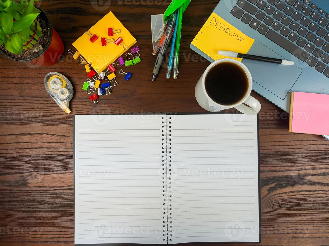 vlak leggen, een bespotten omhoog van een notebook. werkruimte in de achtergrond van de kantoor bureau van de top visie. met wit notitieboekjes, laptops, kantoor benodigdheden, potloden, en koffie cups in de houten bureau. foto