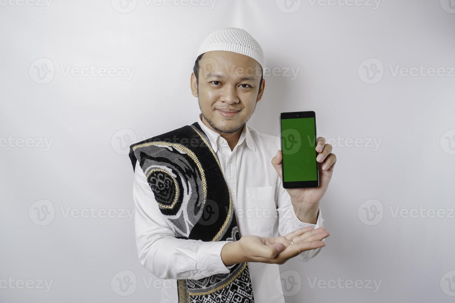 een portret van een gelukkig Aziatisch moslim Mens glimlachen terwijl tonen kopiëren ruimte Aan zijn telefoon, geïsoleerd door wit achtergrond foto