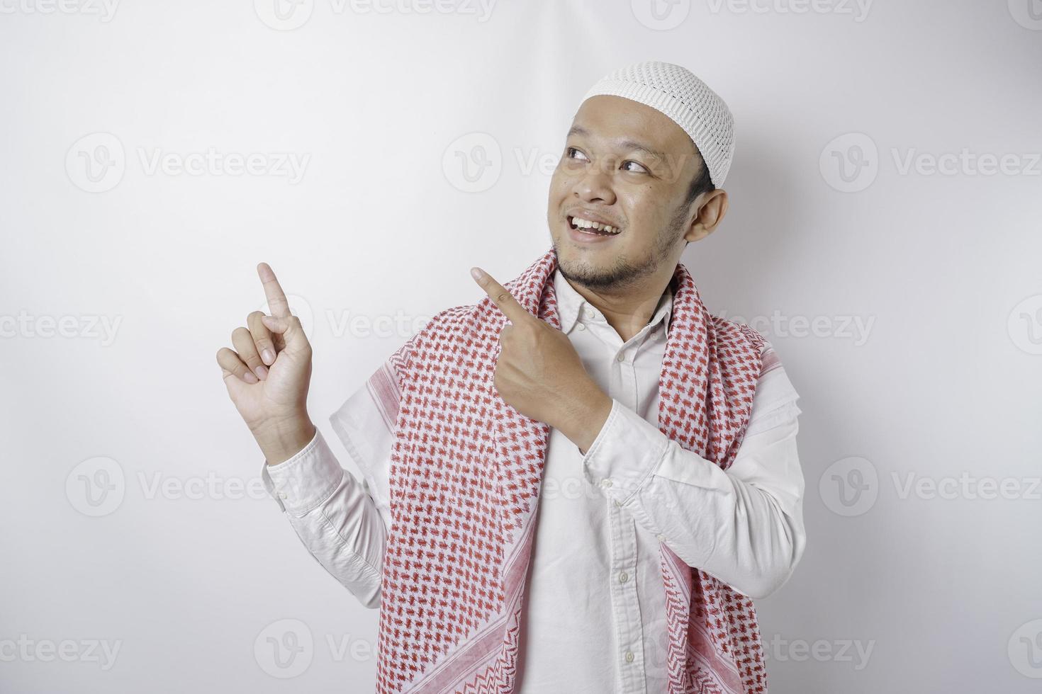opgewonden Aziatisch moslim Mens richten Bij de kopiëren ruimte naast hem, geïsoleerd door wit achtergrond foto
