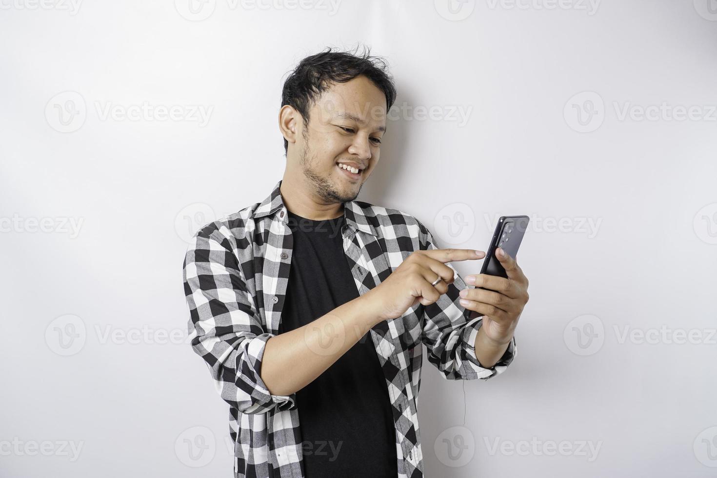 een portret van een gelukkig Aziatisch Mens is glimlachen terwijl Holding Aan zijn telefoon, geïsoleerd door wit achtergrond foto