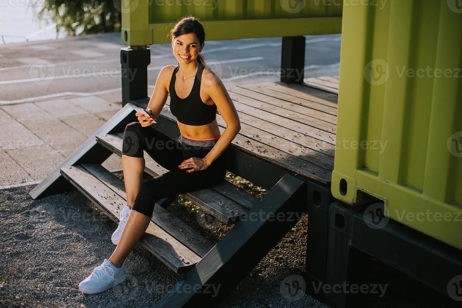 mooi jong vrouw nemen een breken gedurende oefenen buiten en gebruik makend van mobiel telefoon foto