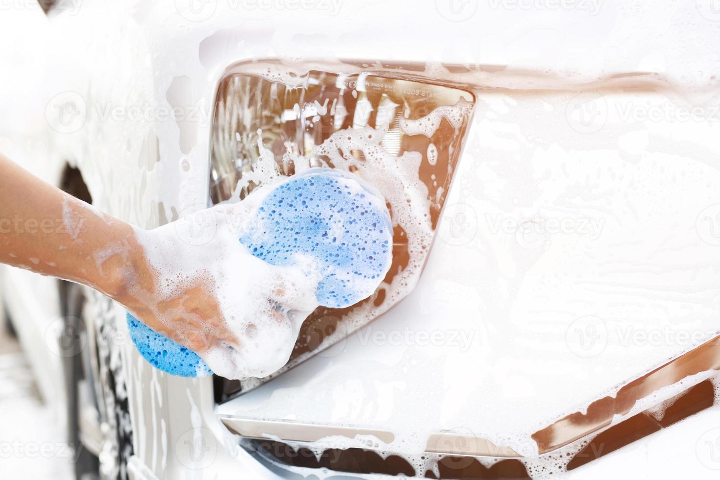 blauwe spons en zeep over de auto om te wassen. motorkap wordt schoongemaakt. concept carwash schoon. foto