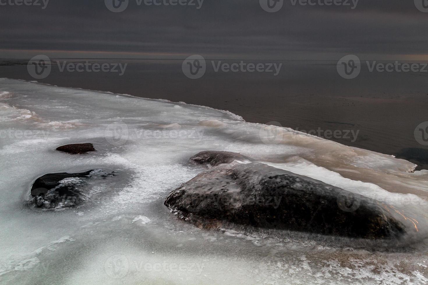 Baltisch zee kust met steentjes en ijs Bij zonsondergang foto