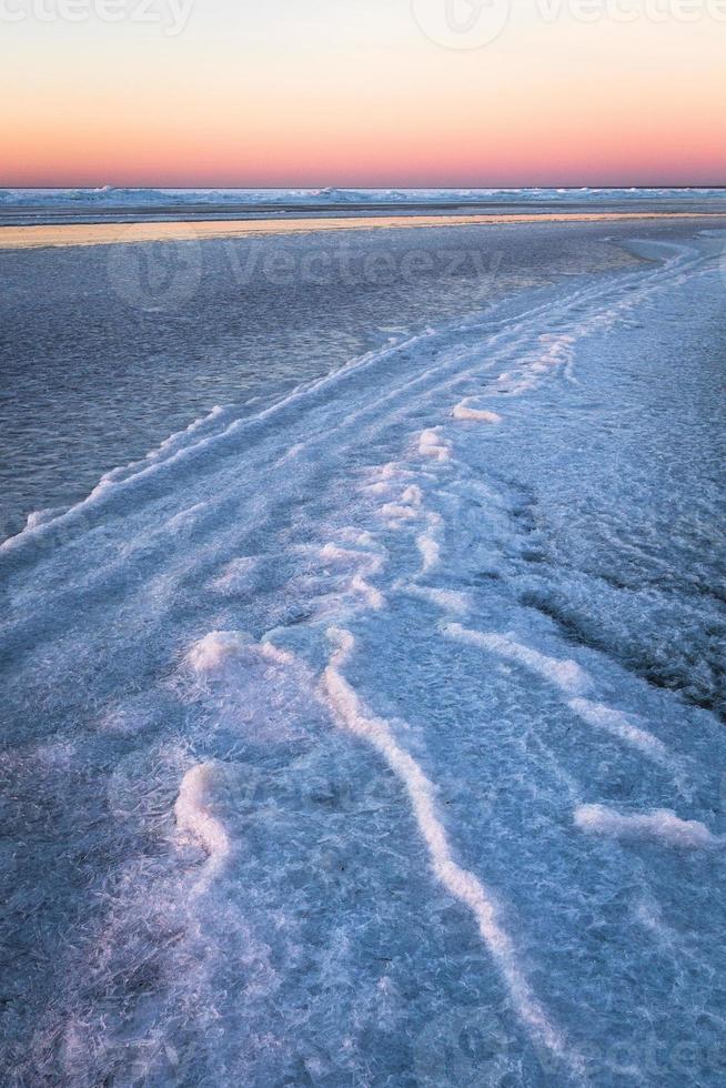 Baltisch zee kust met steentjes en ijs Bij zonsondergang foto