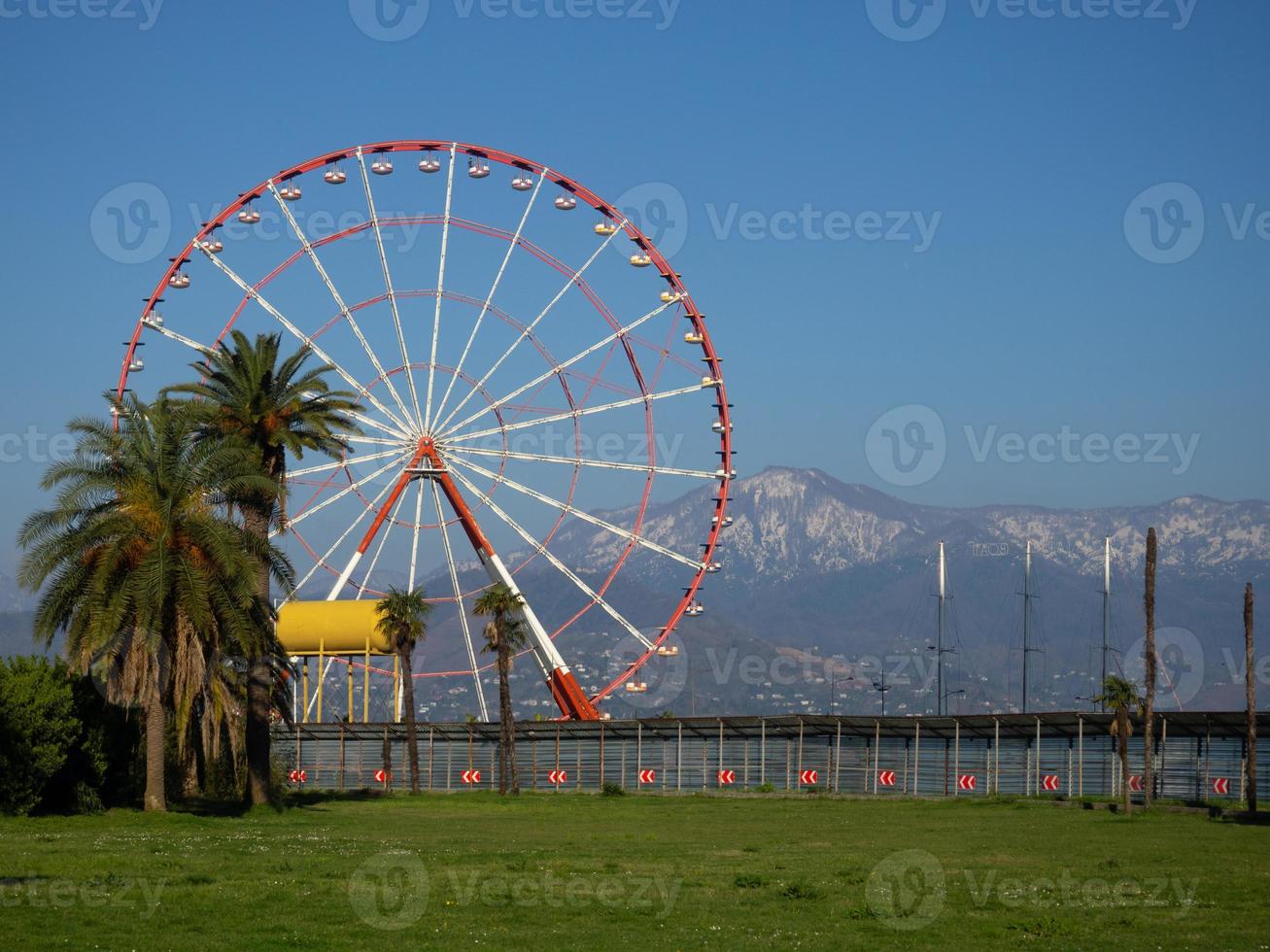 ferris wiel tegen de backdrop van bergen en handpalmen. kust van de zuidelijk stad. amusement park en bergen. foto