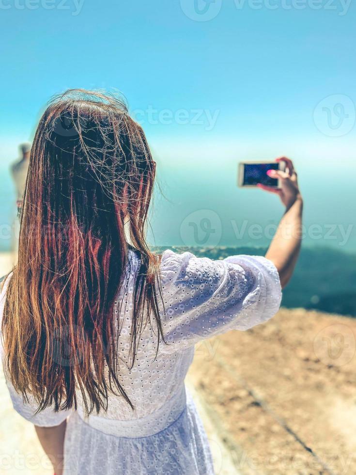 een meisje met donker, lang haar- duurt een selfie tegen de backdrop van bergen. houdt een smartphone in zijn hand- en duurt een afbeelding. afbeelding van uw gezicht foto
