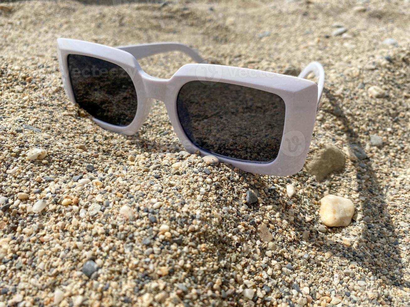 wit plastic zonnebril voor Dames Aan de geel zand van een strand in een warm oostelijk tropisch land zuidelijk paradijs toevlucht foto