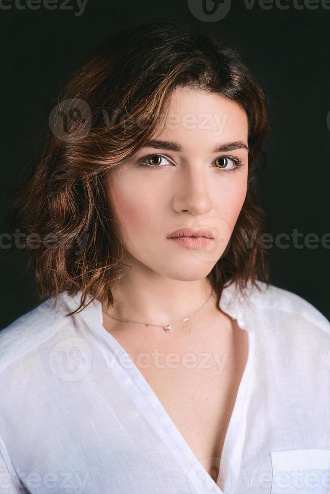 portret van jong, mooi verdrietig actrice met kort bruin haar- in wit overhemd en blauw broek in de studio foto