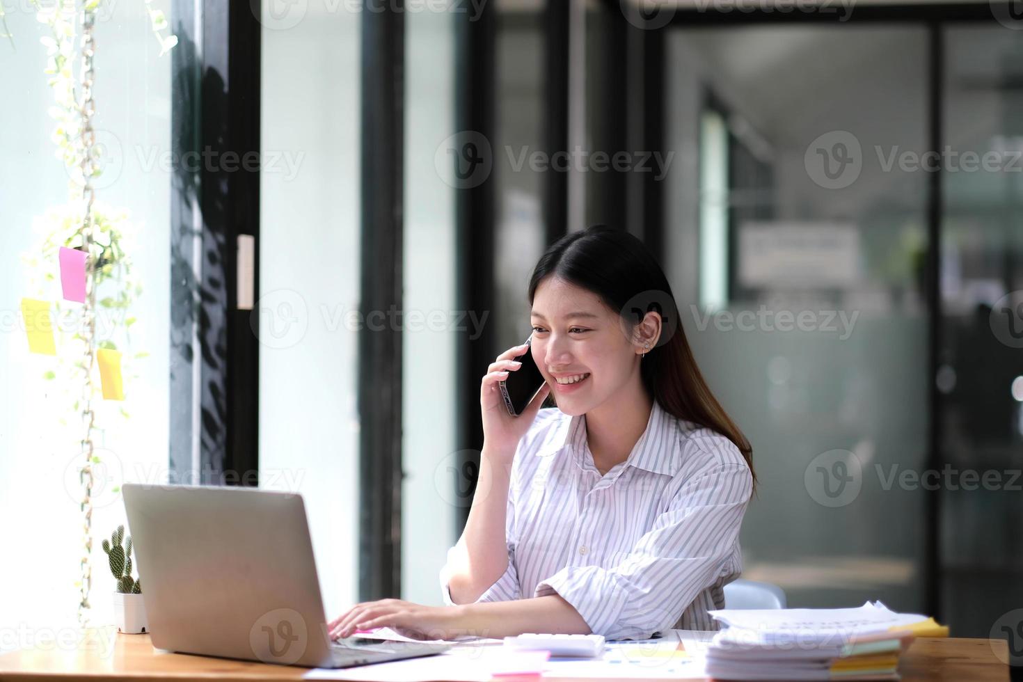 portret van jonge Aziatische zakenvrouw praten op smartphone schrijf notebook laptop in kantoor aan huis. mooi meisje achter de computer op het bureau om de bestelling mee naar huis te nemen. opstarten bedrijf azië vrouw online mkb telemarketing. foto