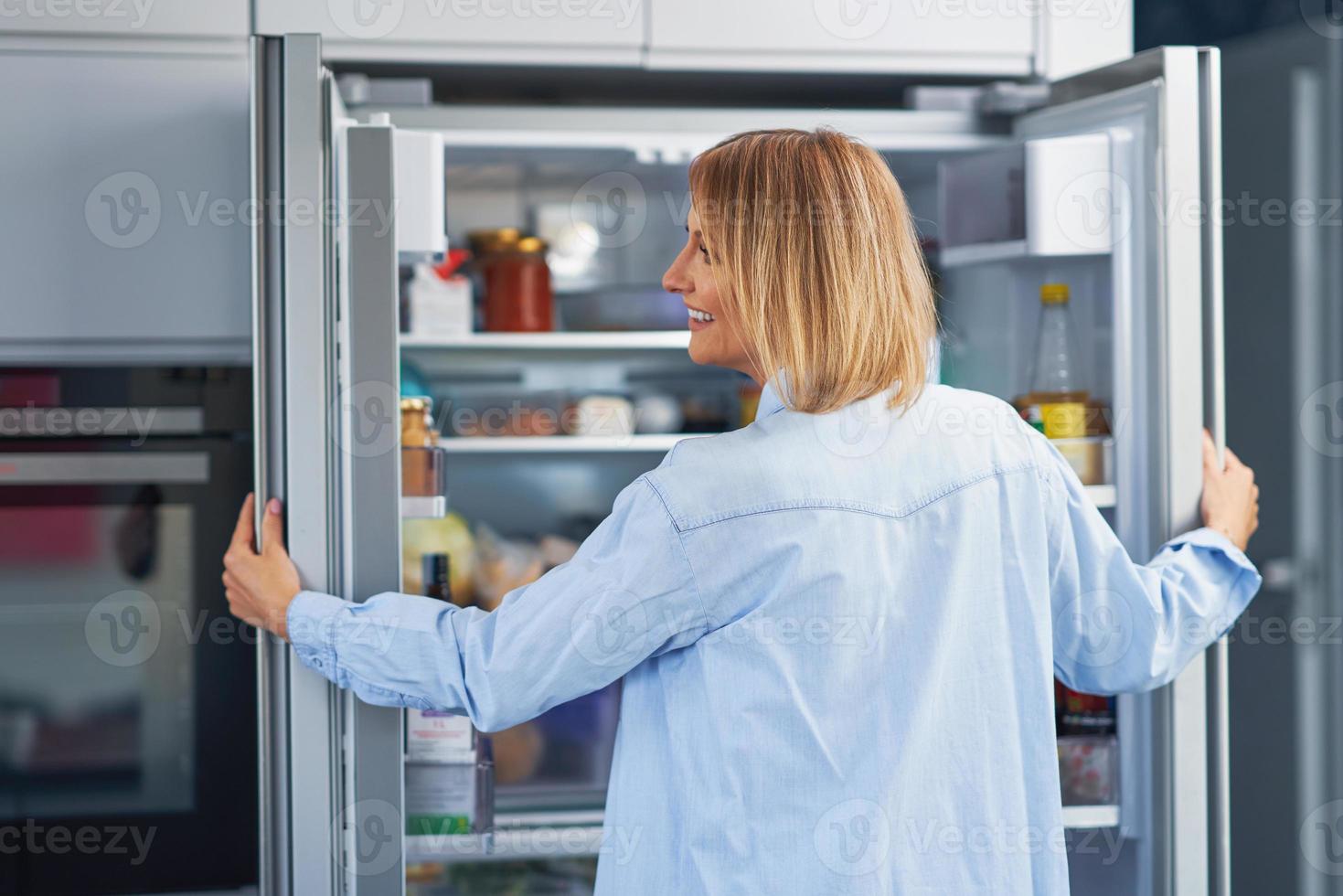 jong volwassen vrouw in de keuken met de koelkast foto