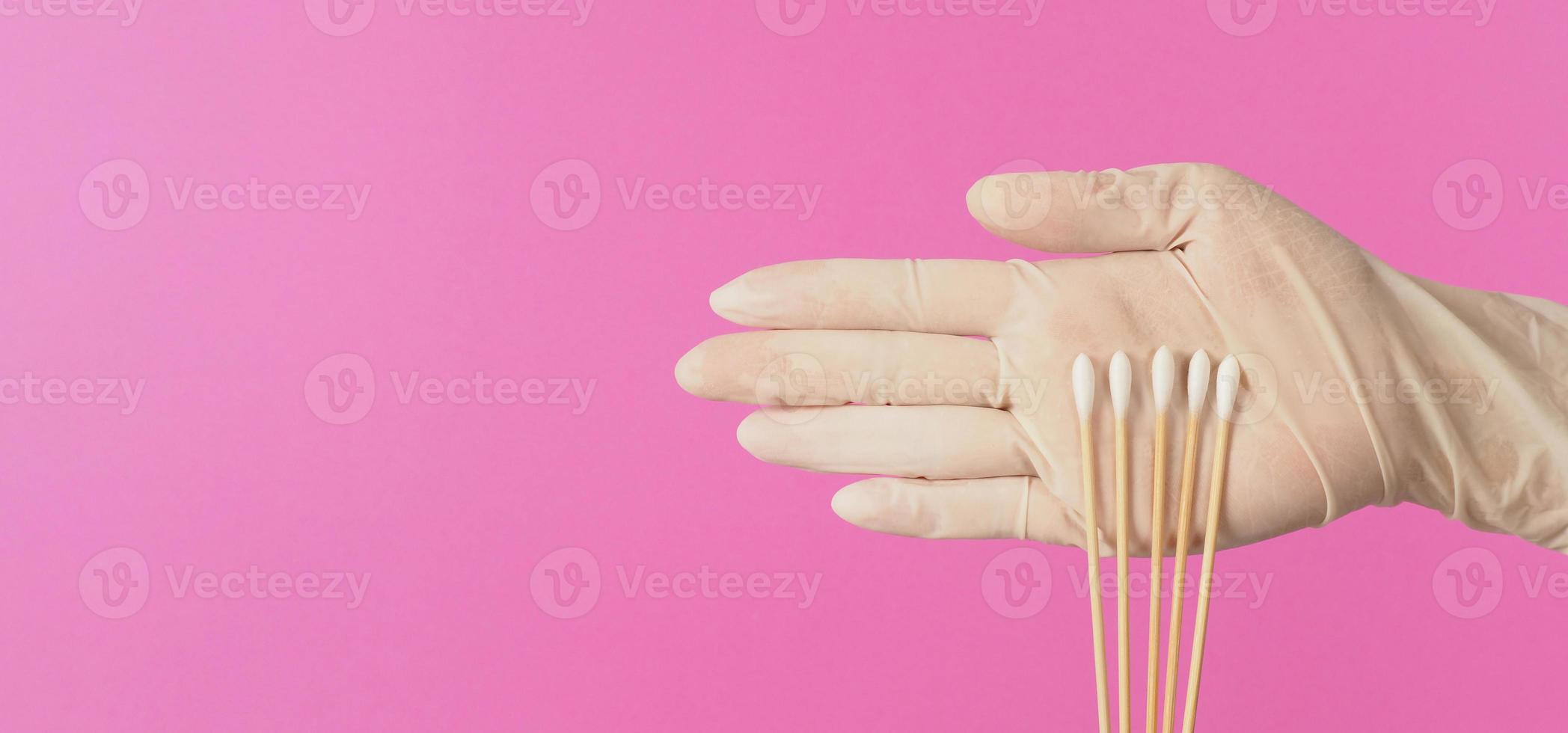 katoen stokjes voor wattenstaafje test in hand- palm met wit medisch handschoenen of latex handschoen Aan roze achtergrond. foto