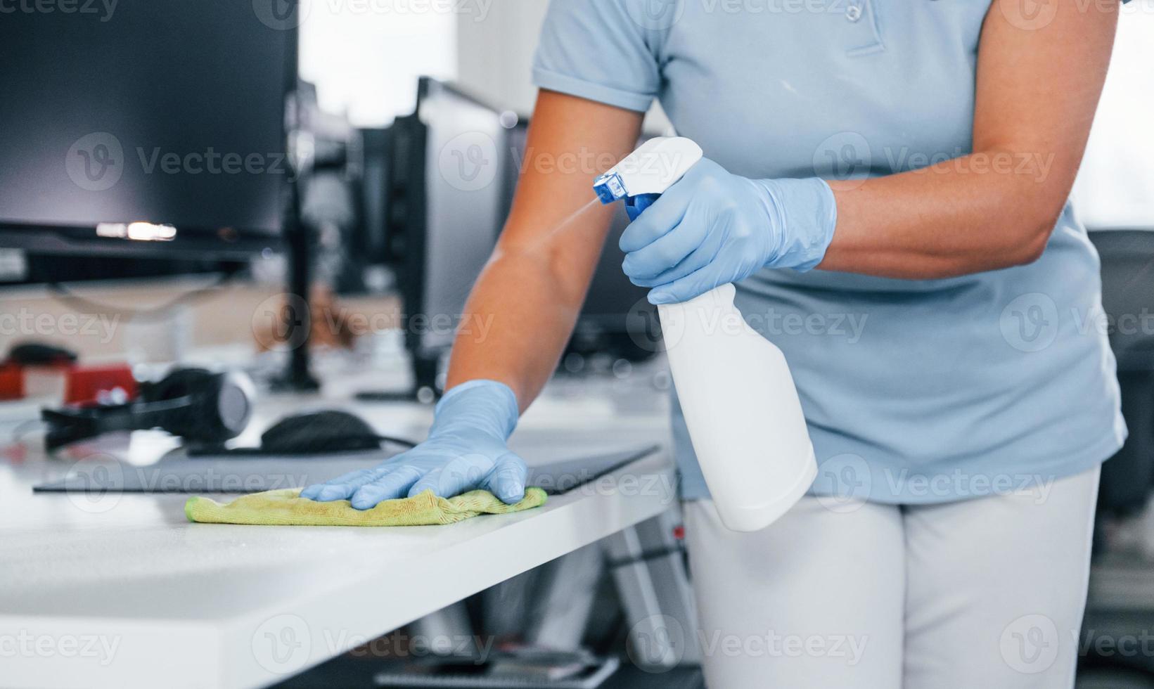 dichtbij omhoog visie van vrouw in beschermend handschoenen dat schoonmaak tafels in de kantoor foto