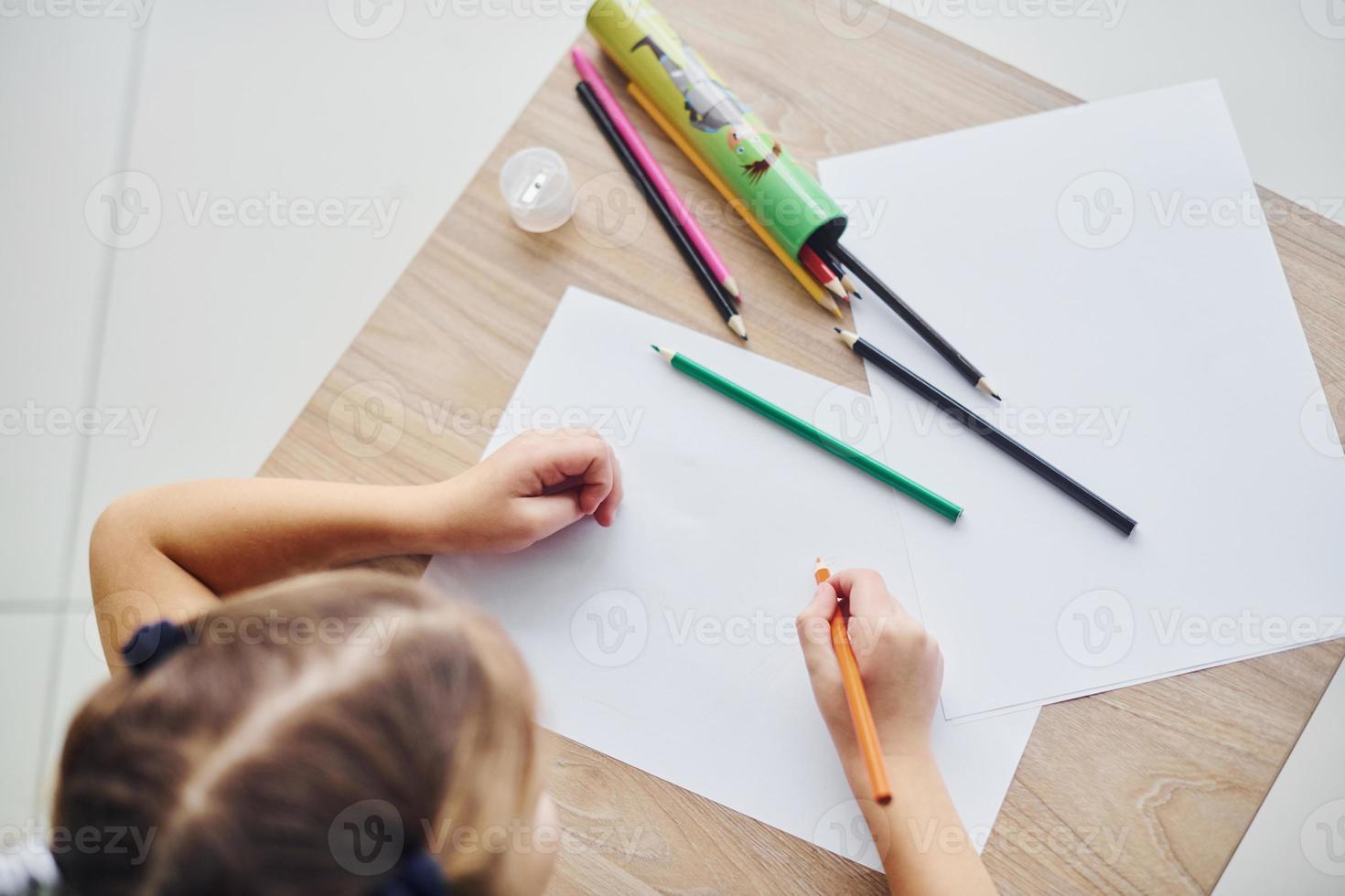 top visie van weinig meisje met potloden en leeg papier vel Aan de tafel foto