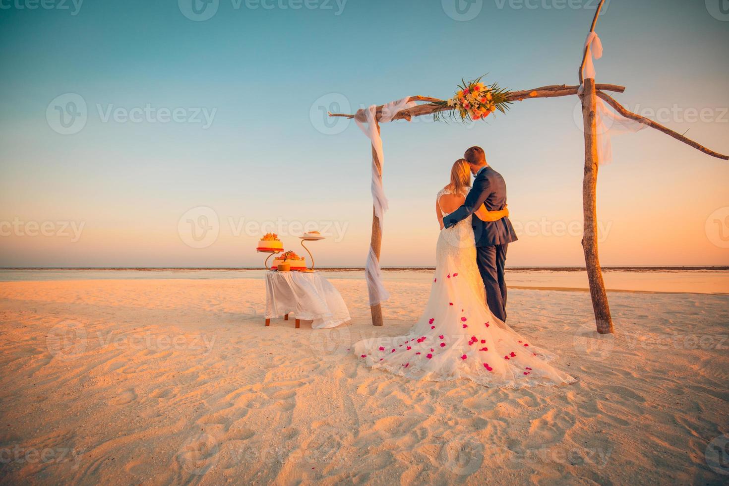 de bruid en bruidegom onder boog Aan strand. romantisch bruiloft achtergrond. bruid en bruidegom romantisch pasgetrouwden, huwelijksreis Aan de strand zonsondergang concept foto