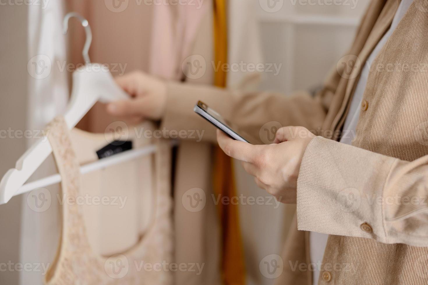 vrouw Holding smartphone en nemen foto van haar oud kleren naar verkopen hen online. verkoop Aan website, e-commerce. hergebruik, tweedehands concept. bewust klant, duurzame levensstijl. detailopname visie.