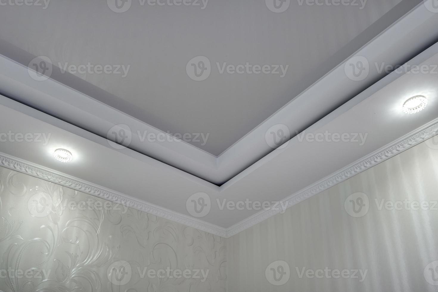 geschorst plafond met halogeen vlekken lampen en gipsplaat bouw met ingewikkeld kroon gieten in leeg kamer in appartement of huis. rekken plafond wit en complex vorm geven aan. foto