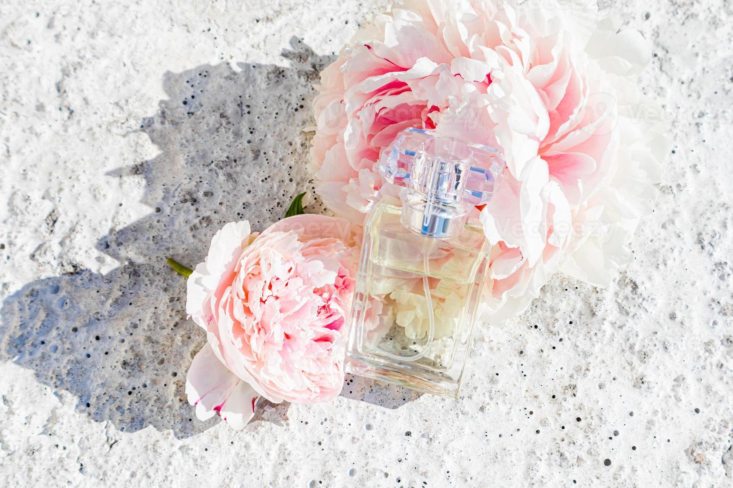 een glas fles van vrouwen parfum of toilet water leugens Aan roze pioenen en een grijs beton achtergrond. de concept van parfumerie en schoonheid. foto