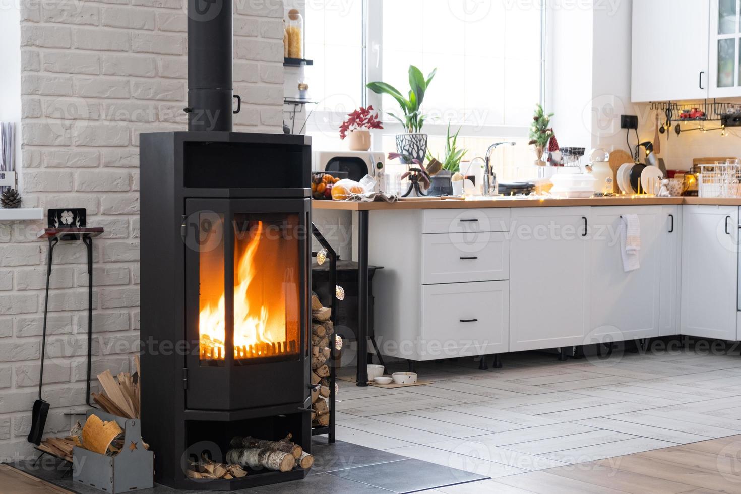 feestelijk interieur van huis is versierd voor Kerstmis en nieuw jaar in zolder stijl met zwart fornuis, haard, Kerstmis boom. warm studio kamer met wit keuken, brandend hout, knus en verwarming van huis foto