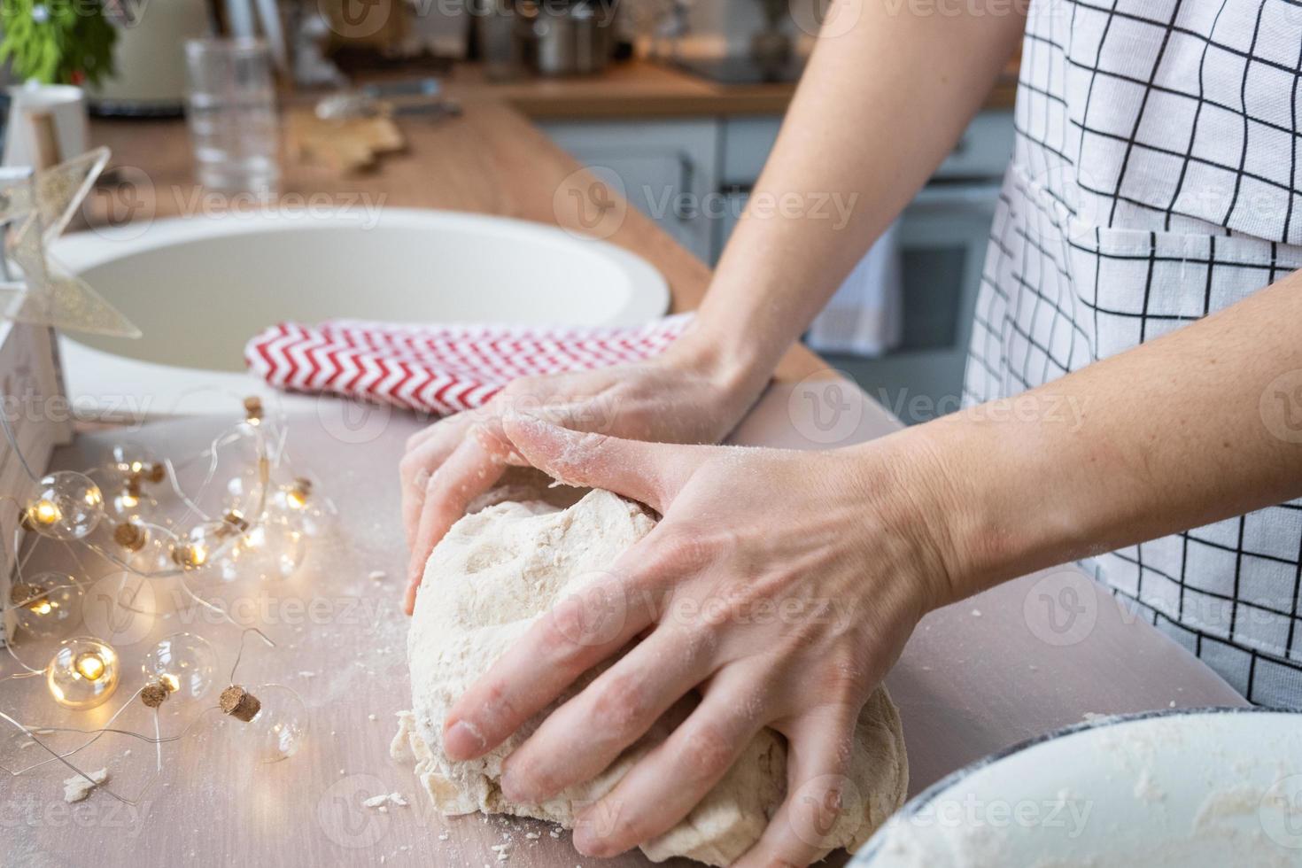 handen kneden dik deeg Aan de keuken tafel, versierd met feestelijk decoraties voor Kerstmis en nieuw jaar. bakken Bij huis, aroma en comfort. detailopname foto