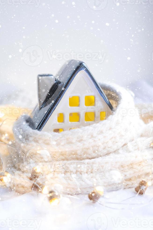 gezellig huis is gewikkeld in een muts en sjaal in een sneeuwstorm - vensterbank decor. winter, sneeuw - woningisolatie, bescherming tegen kou en slecht weer, kamerverwarmingssysteem. feestelijke stemming, kerstmis, nieuwjaar foto