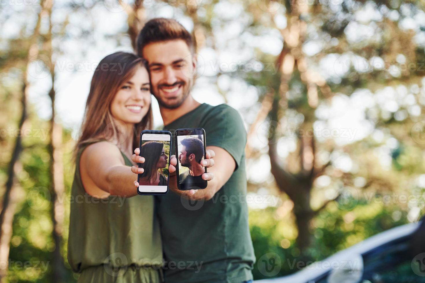 Holding twee smartphones met foto's van hen. mooi jong paar hebben een mooi zo tijd in de Woud Bij dag foto