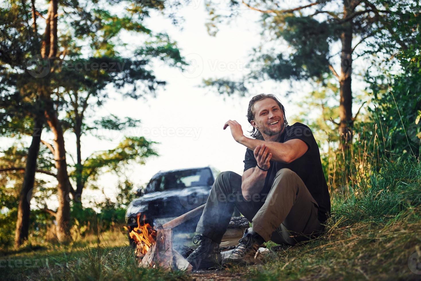 tijd voor een rust uit. Mens in zwart overhemd in de buurt de kampvuur in de Woud Bij zijn weekend tijd foto