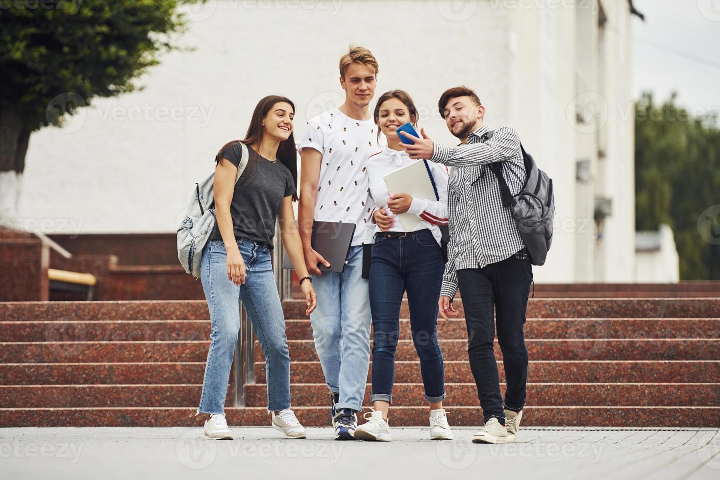 pratend selfie terwijl hebben een wandelen. groep van jong studenten in gewoontjes kleren in de buurt Universiteit Bij dag foto