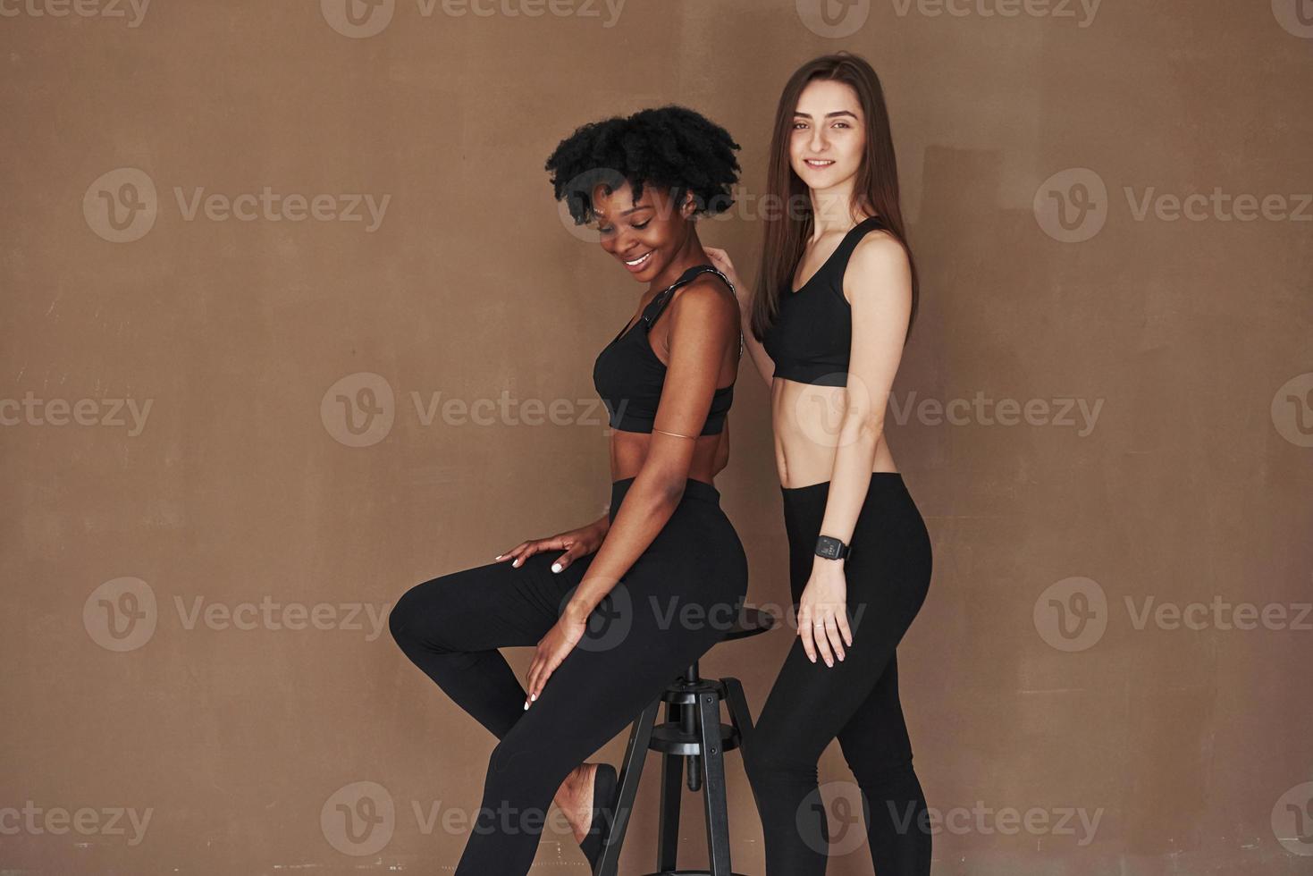 modieuze jeugd. twee multi-etnische vriendinnen staan in de studio met bruine achtergrond foto