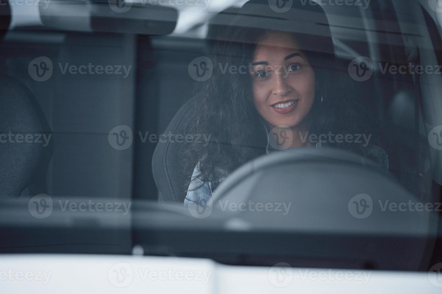 schattig meisje met zwart haar probeert haar gloednieuwe dure auto in de autosalon foto