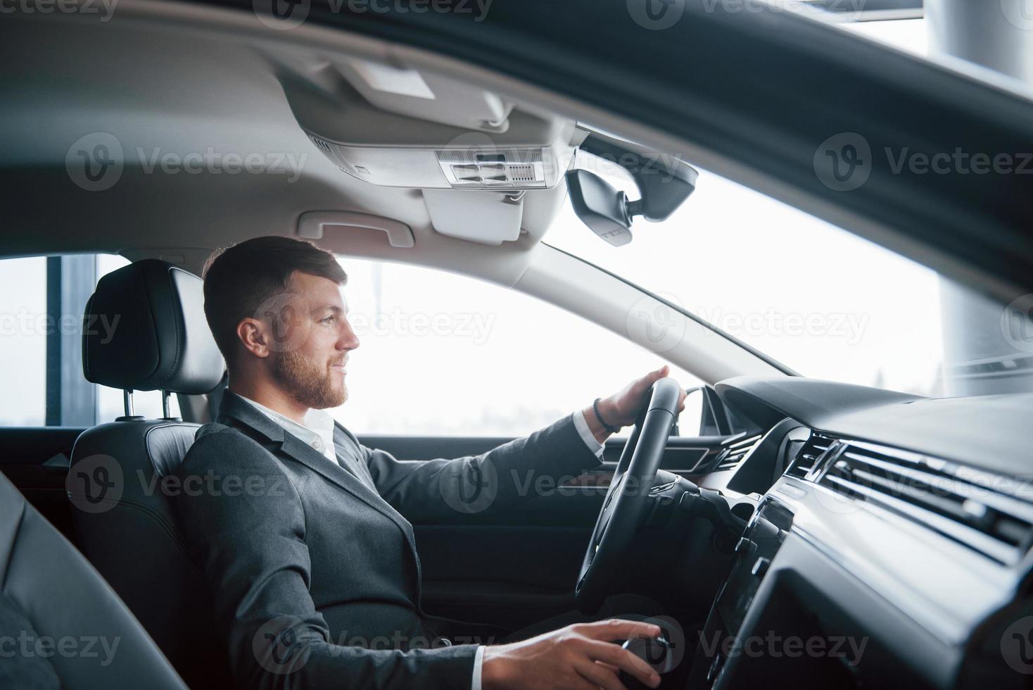 oprechte glimlach. moderne zakenman die zijn nieuwe auto in de autosalon probeert foto