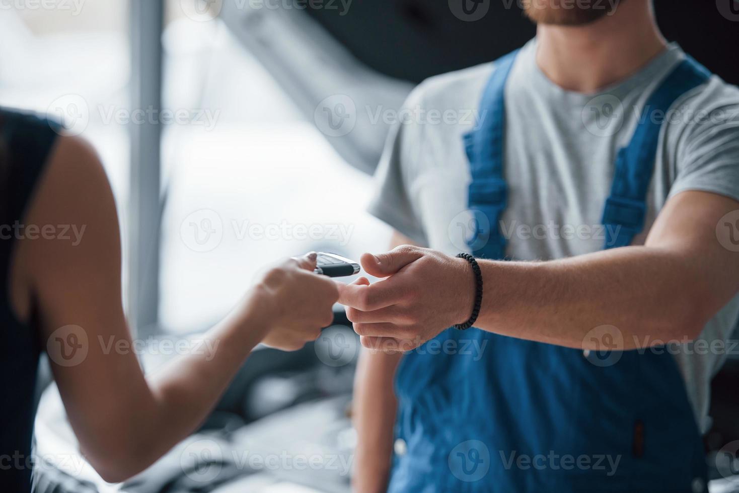 proces van het geven van de sleutels. vrouw in de autosalon met werknemer in blauw uniform die haar gerepareerde auto terugneemt foto