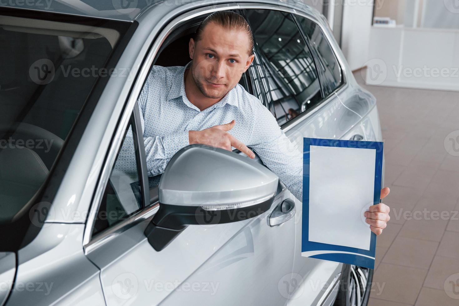 document tonen. manager zit in moderne witte auto met papier in handen foto