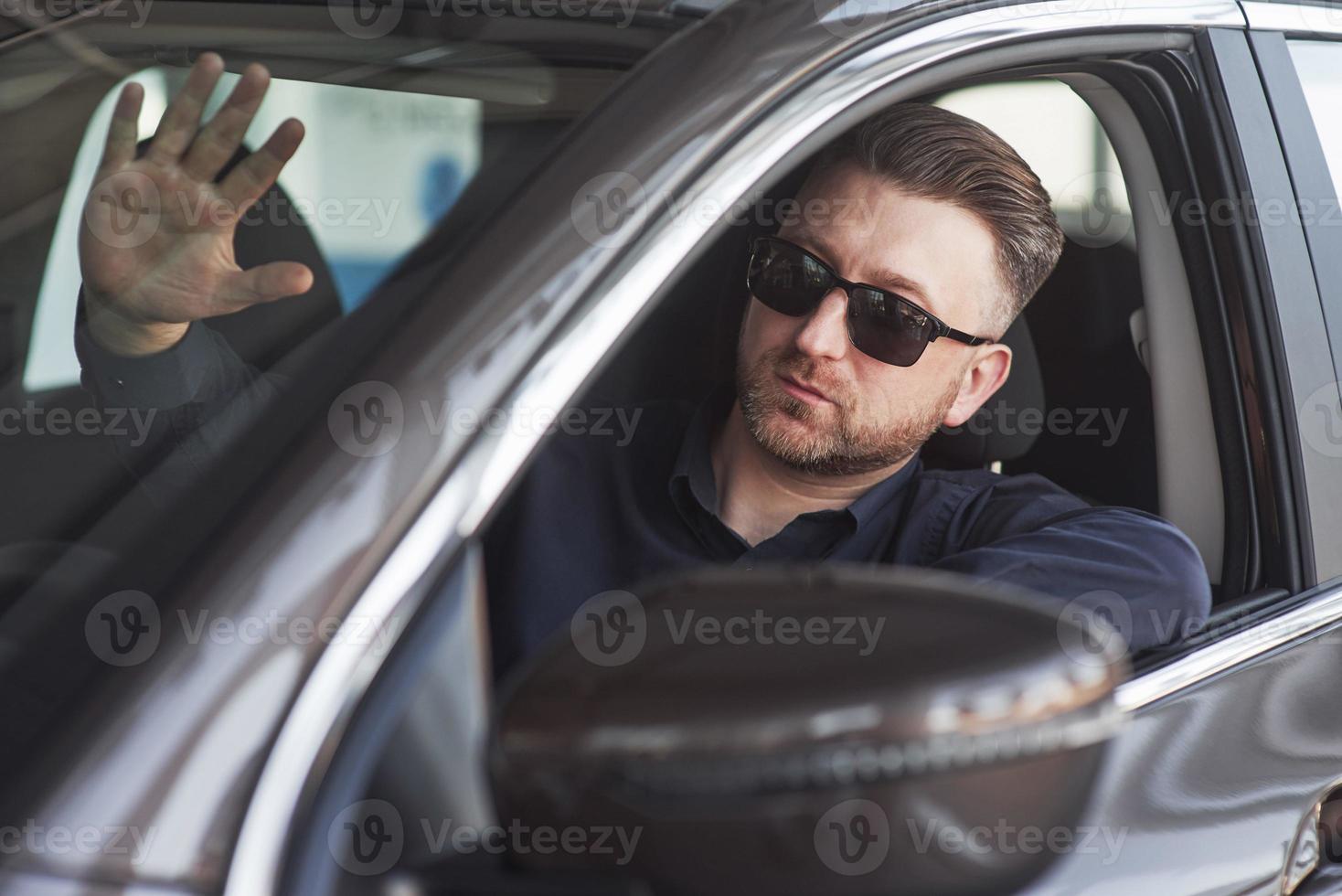 Hallo, gebaar. Mens in officieel kleren proberen zijn nieuw auto in auto- salon foto