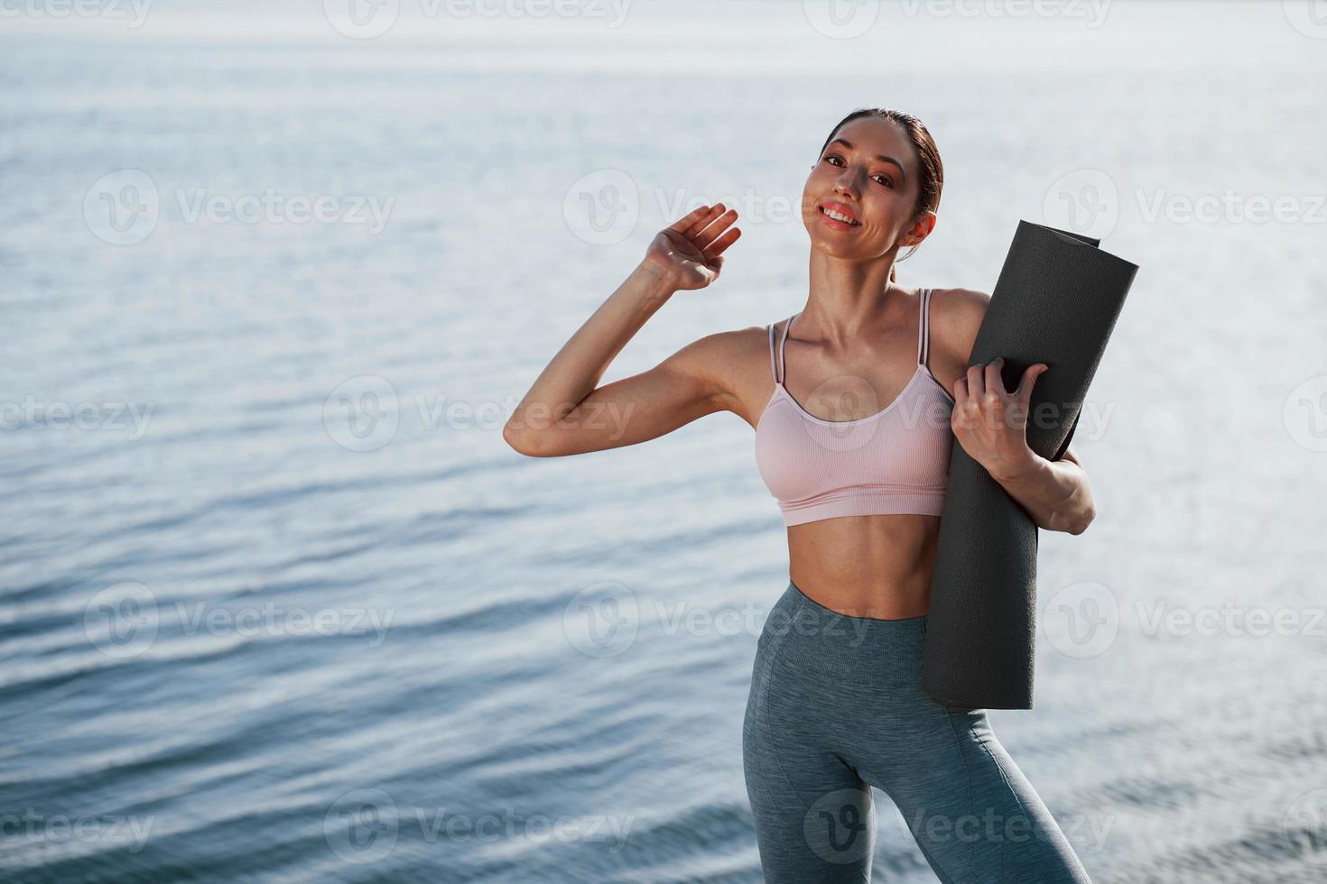Hallo, gebaar. meisje in sportief kleren staat tegen water Aan achtergrond foto