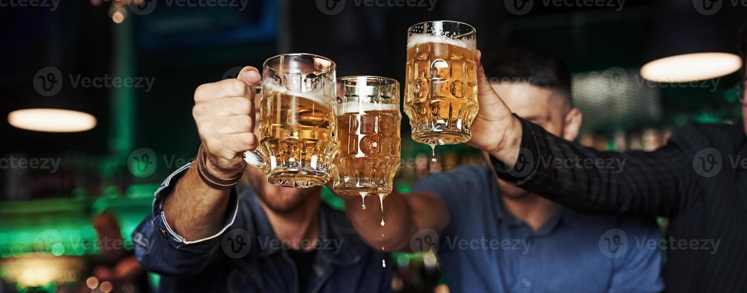 kloppen bril. drie sport- fans in een bar aan het kijken voetbal. met bier in handen foto