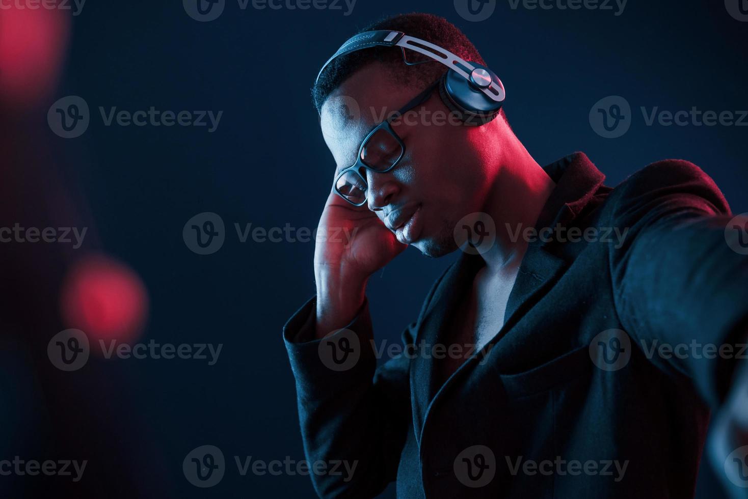 genieten van luisteren muziek- in koptelefoon. in bril. futuristische neon verlichting. jong Afrikaanse Amerikaans Mens in de studio foto
