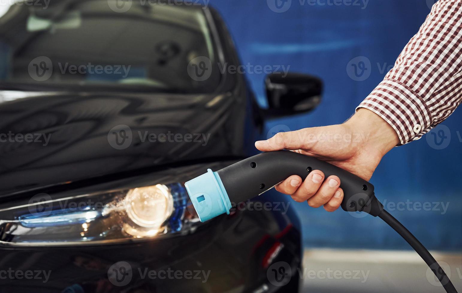 Mens staat tegen een elektrisch auto en houdt de opladen kabel foto