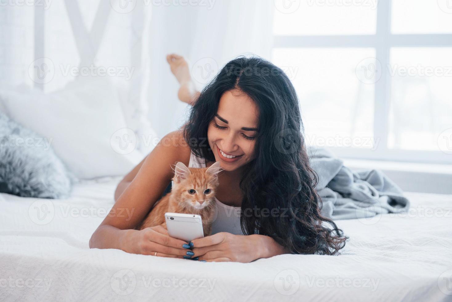 kat liefdes naar worden in de buurt deze meisje. aantrekkelijk blond resting Aan de wit bed met haar schattig katje foto