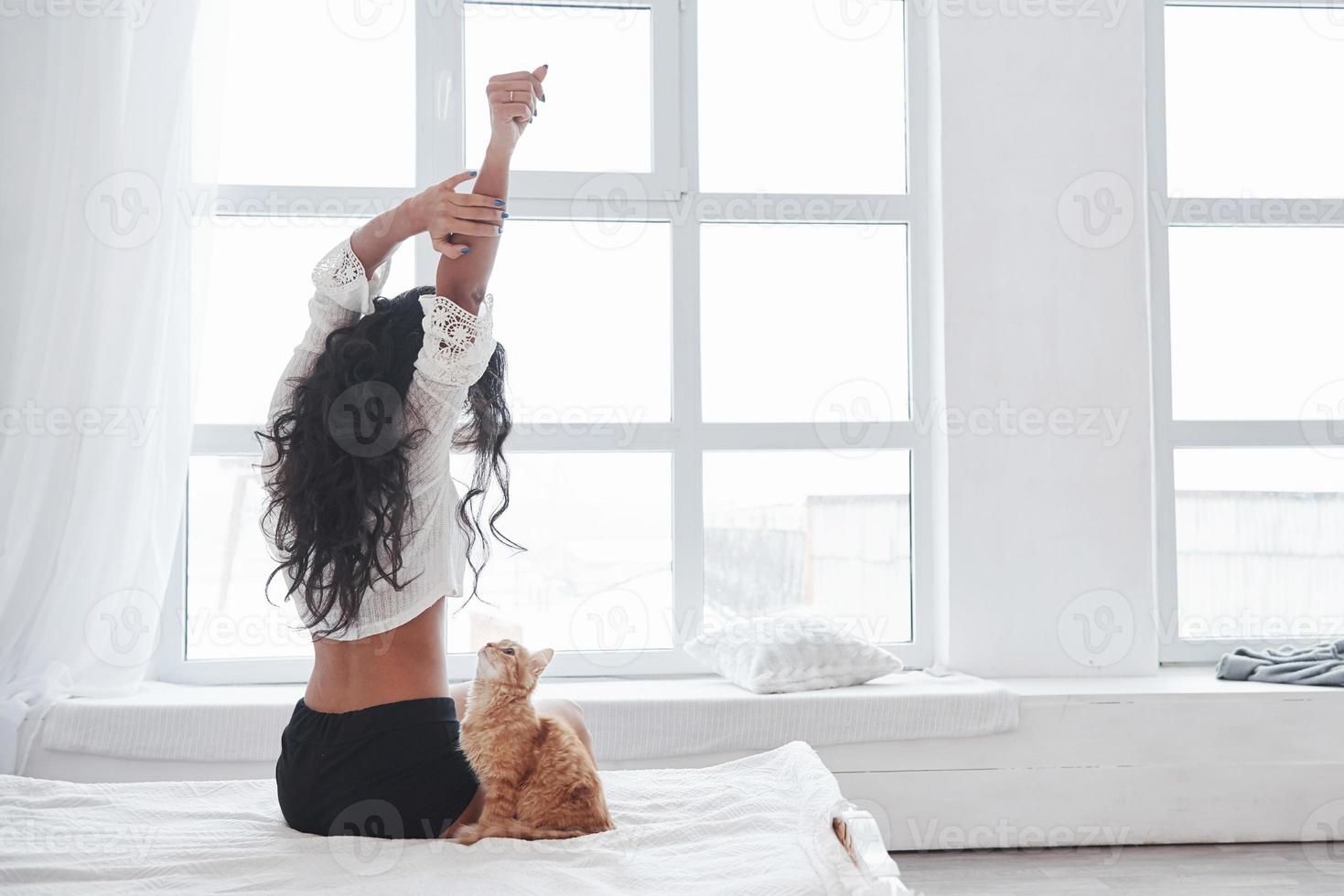 ochtend- strekt zich uit. aantrekkelijk blond resting Aan de wit bed met haar schattig katje foto