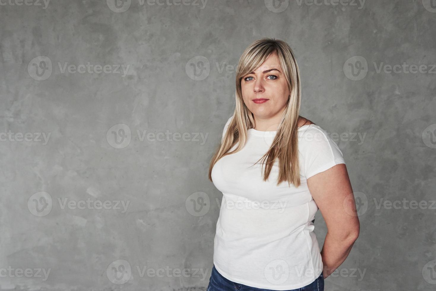 gewoontjes kleren. jong wit vrouw in de studio staand tegen grijs achtergrond foto