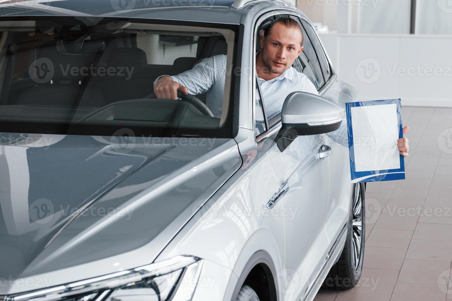 duur auto. manager zittend in modern wit auto met papier en documenten in handen foto