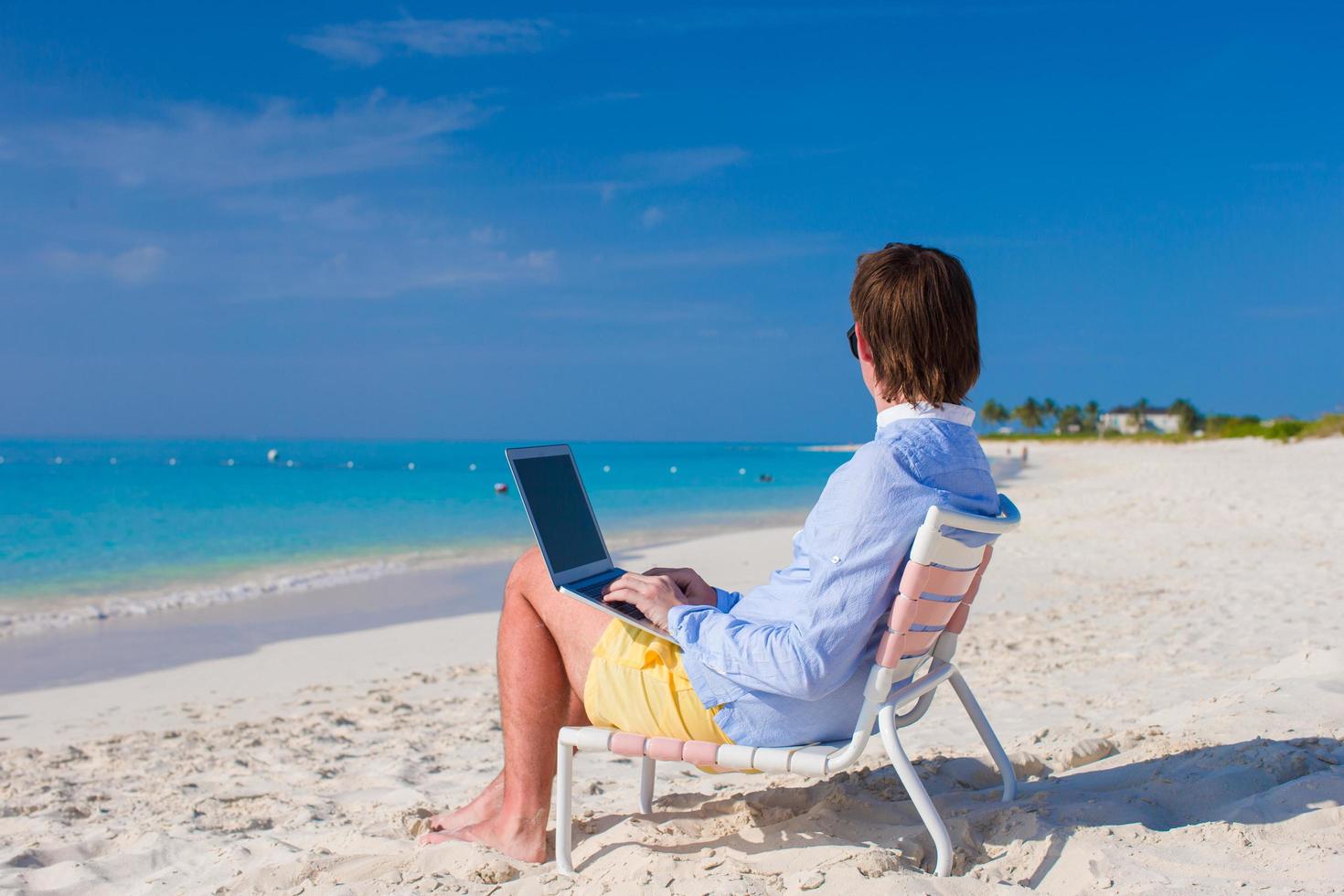 man met een laptop op een tropisch strand foto