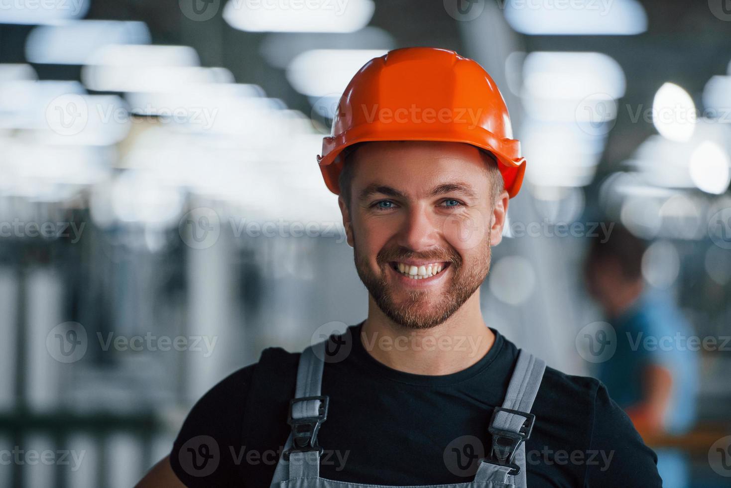 glimlachen en gelukkig medewerker. portret van industrieel arbeider binnenshuis in fabriek. jong technicus met oranje moeilijk hoed foto