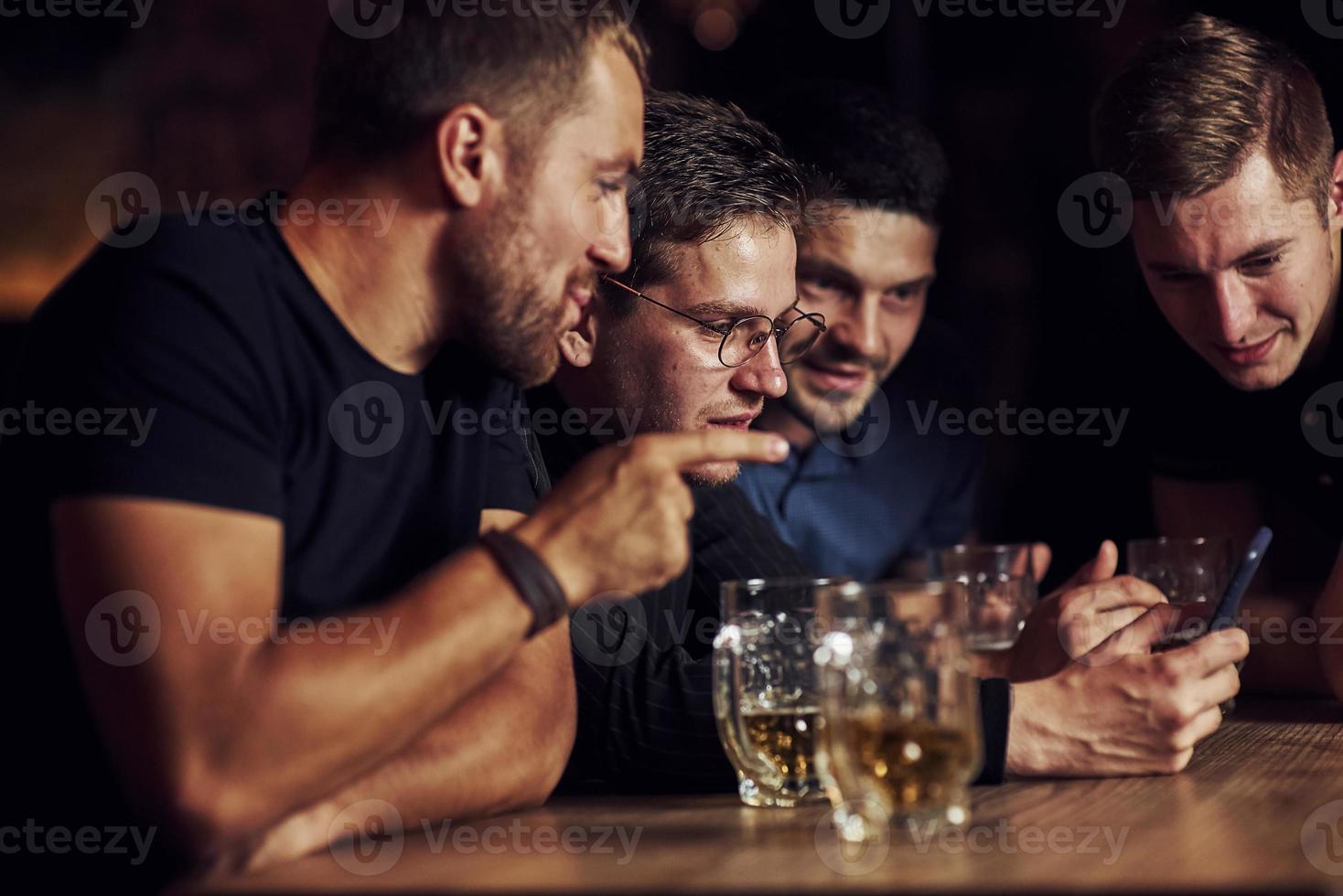 grappig inhoud Aan smartphone. drie vrienden resting in de kroeg met bier in handen. hebben gesprek foto
