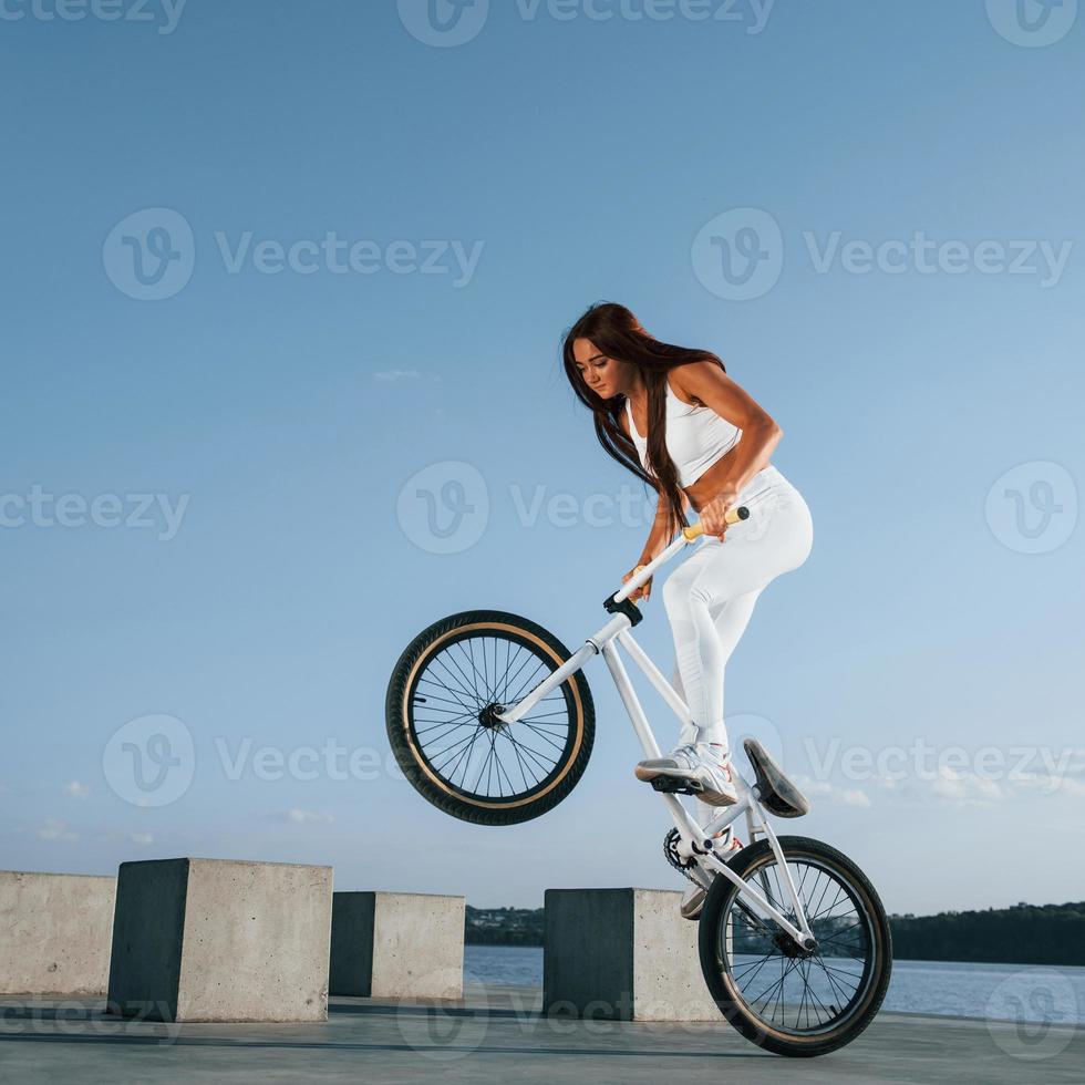 aan het doen stunten. vrouw rijder is Aan de fiets Bij dag in de buurt de meer. geschiktheid vrouw in sportief kleren foto