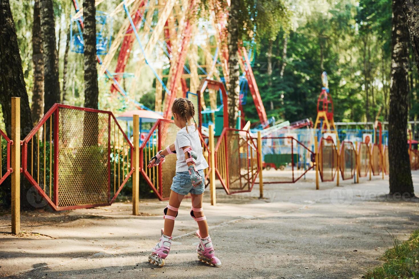 achterzijde visie. vrolijk weinig meisje Aan rol skates hebben een mooi zo tijd in de park in de buurt attracties foto