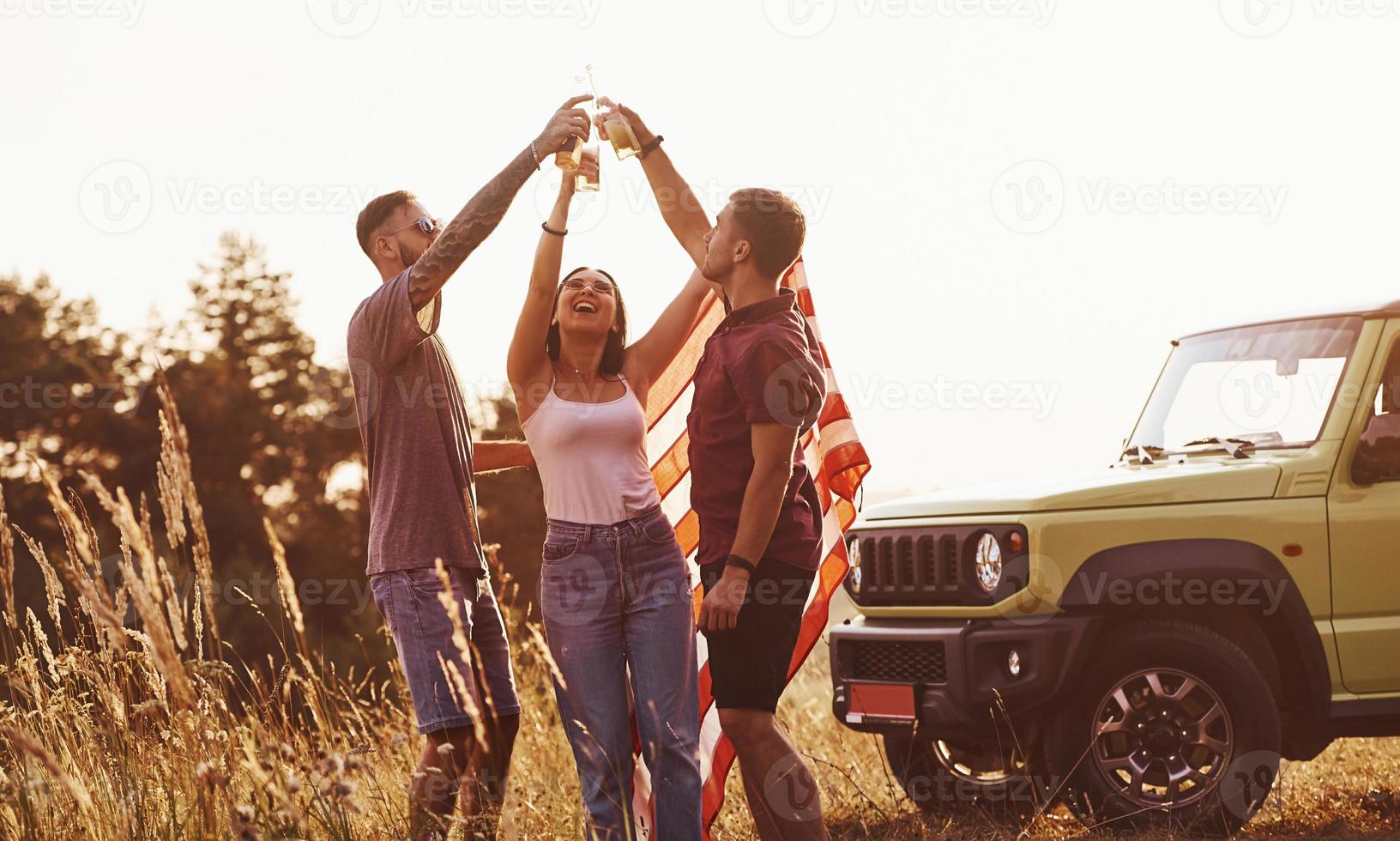 geven proost. vrienden hebben mooi hoor weekend buitenshuis in de buurt van hen groen auto met Verenigde Staten van Amerika vlag foto