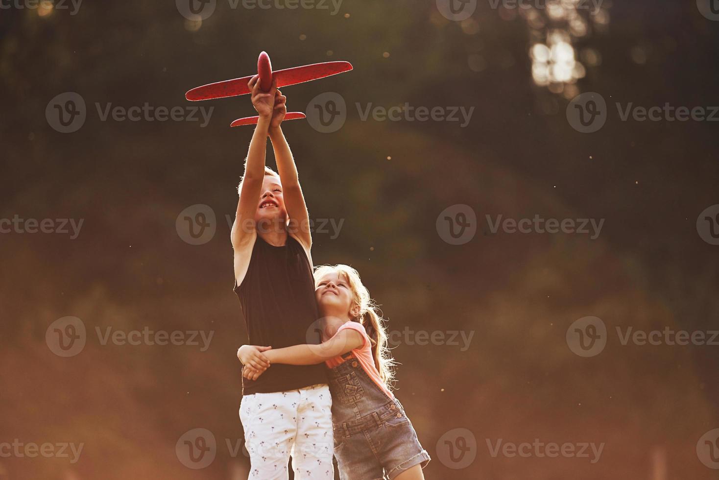 meisje en jongen hebben pret buitenshuis met rood speelgoed- vliegtuig in handen foto