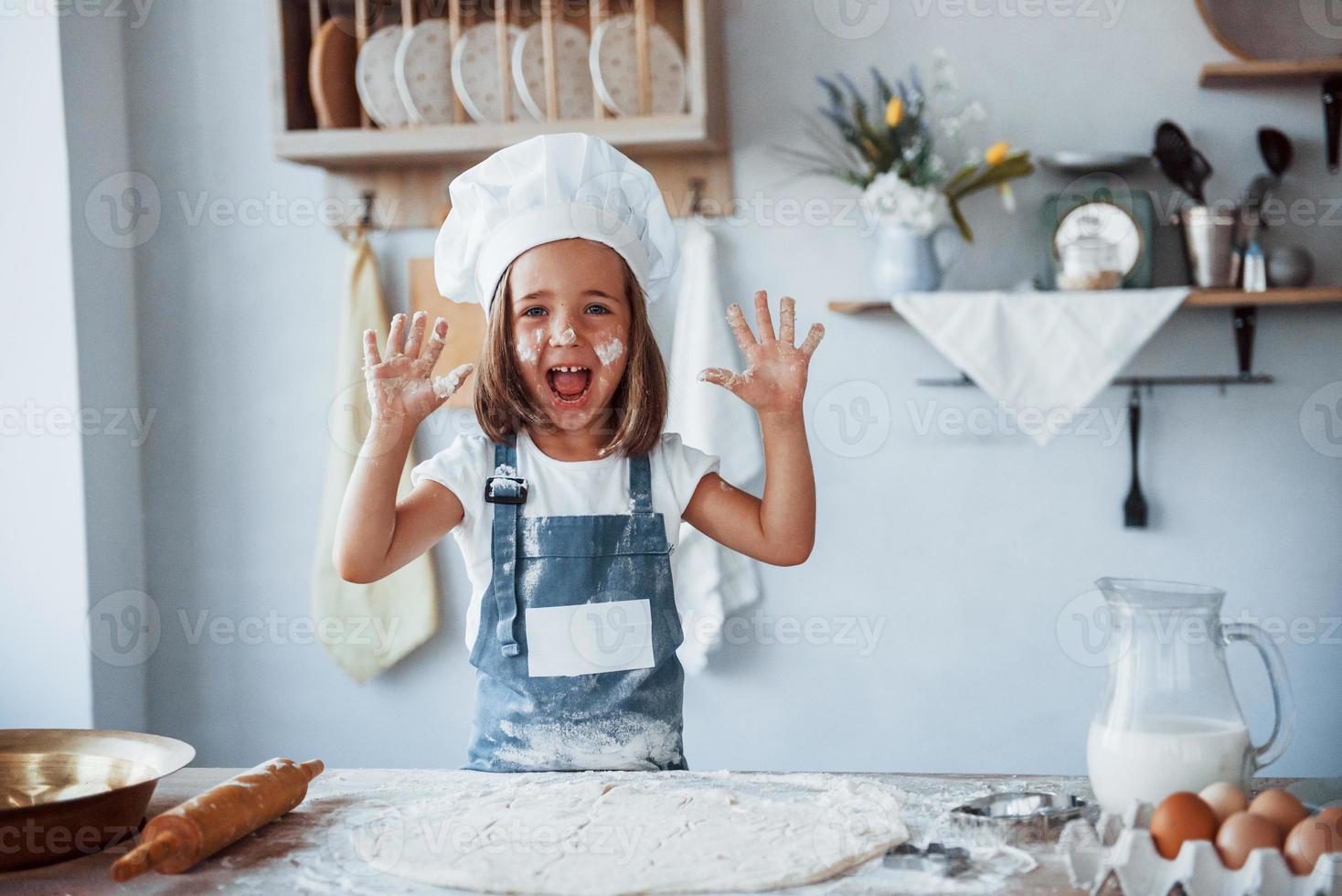 hebben plezier. schattig kind in wit chef uniform voorbereidingen treffen voedsel Aan de keuken foto