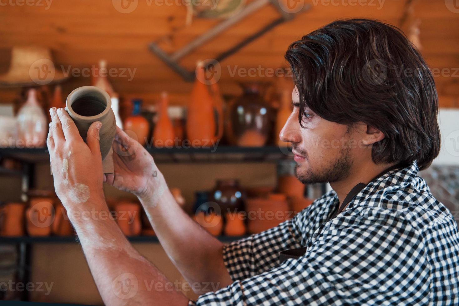 jong keramist houdt vers handgemaakt pot in hand- en looks Bij resultaten van zijn werk foto